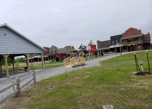 A playground and western-style buildings in a grassy area, with a cloudy sky overhead.