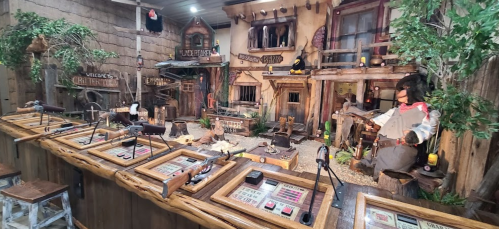 A western-themed shooting gallery with targets, props, and a rustic backdrop featuring a saloon and cowboy figures.