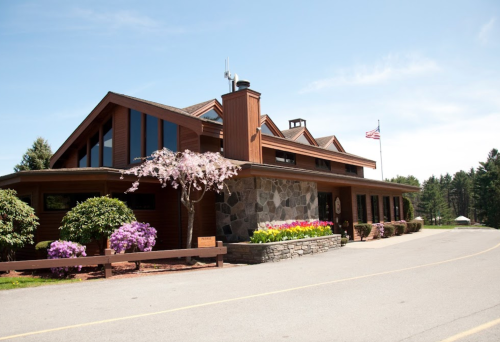 A modern building with a stone facade, surrounded by blooming flowers and trees, under a clear blue sky.