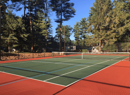 A tennis court surrounded by trees, featuring a green surface and red lines under a clear blue sky.