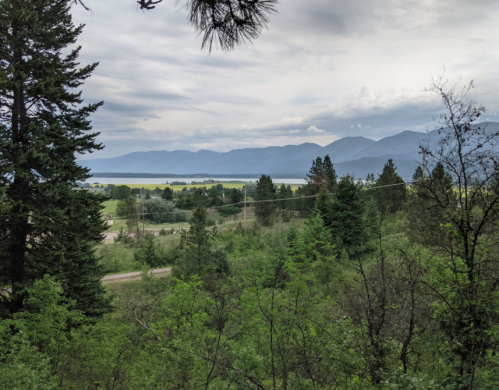 A scenic view of a lake surrounded by mountains and lush greenery under a cloudy sky.