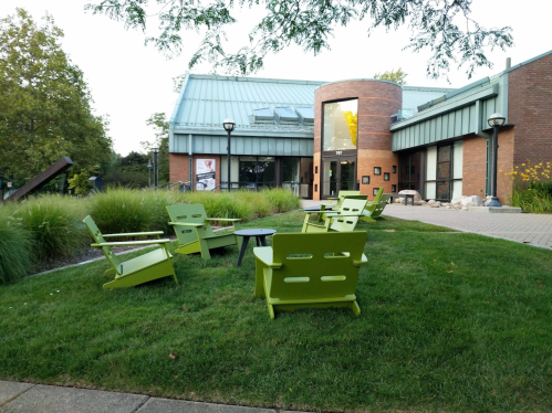 A green lawn with modern green chairs and a table in front of a brick building with large windows.