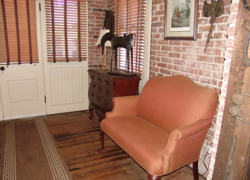 Cozy entryway featuring a brick wall, an orange sofa, wooden floor, and decorative items on a chest of drawers.