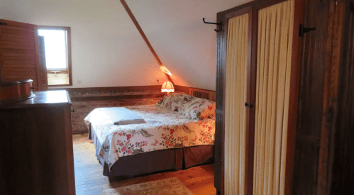 Cozy bedroom with a floral bedspread, wooden furniture, and warm lighting from a lamp.