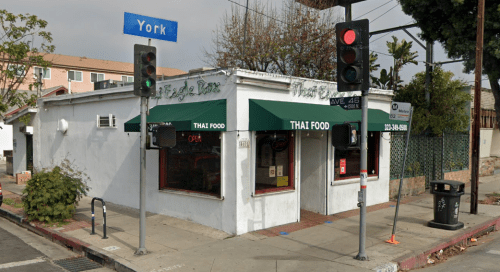 A small Thai food restaurant on a street corner with green awnings and a traffic light nearby.
