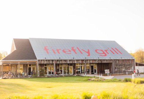 Exterior of Firefly Grill, a rustic building with a large red sign, surrounded by green grass and trees.