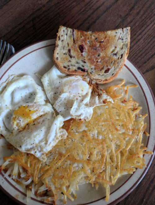 A plate with two fried eggs, crispy hash browns, and a slice of toasted bread with cranberries.