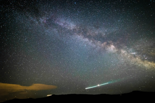 A stunning night sky filled with stars and the Milky Way, with a bright comet streaking across the horizon.