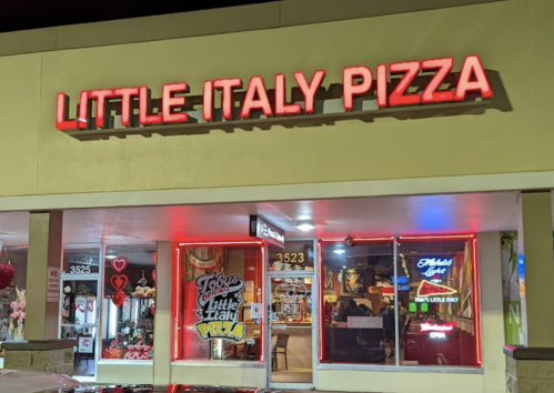 A brightly lit storefront of Little Italy Pizza, featuring neon signs and a welcoming atmosphere at night.