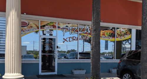 Exterior of Pizza Xtreme restaurant with large windows displaying menu items and an "Open" sign.