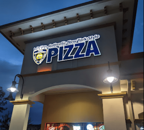 Sign for NYPD Authentic New York Style Pizza illuminated at dusk, featuring a badge logo and bright lettering.