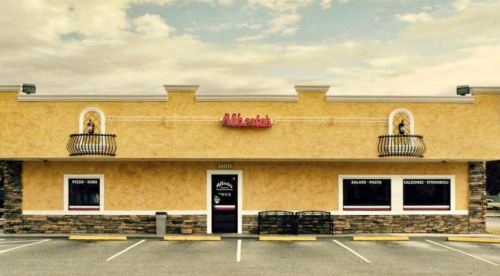 Exterior of a restaurant named "Alberto's," featuring a yellow facade, decorative balconies, and a sign with menu items.