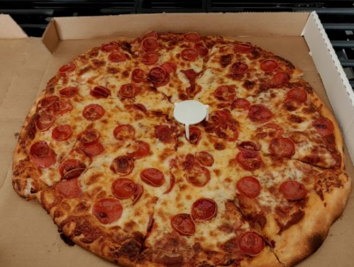 A large pizza with pepperoni slices and melted cheese, in a pizza box with a white pizza saver in the center.