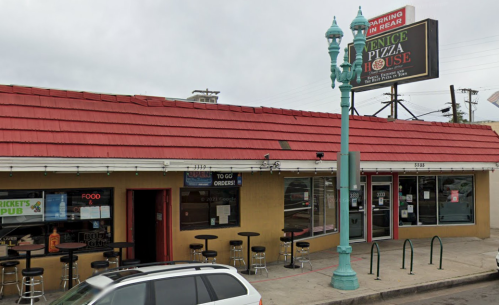 Exterior of Venice Pizza House with a red roof, outdoor seating, and a sign indicating parking in the rear.