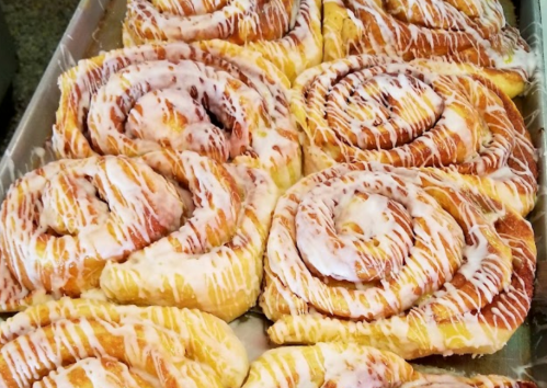 A tray of freshly baked cinnamon rolls drizzled with white icing, showcasing their swirled, golden-brown layers.