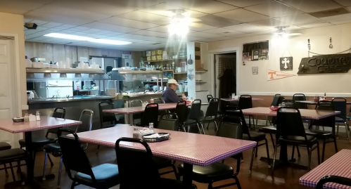A cozy diner with checkered tables, empty chairs, and a kitchen in the background, creating a quiet atmosphere.
