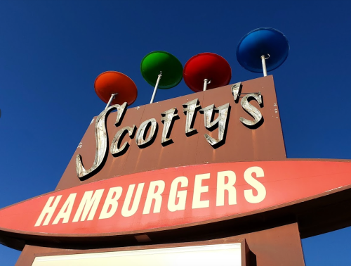 Sign for Scotty's Hamburgers featuring colorful round signs on top against a clear blue sky.