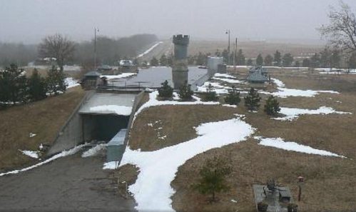 A foggy landscape featuring a military bunker, tower, and patches of snow on grassy terrain.