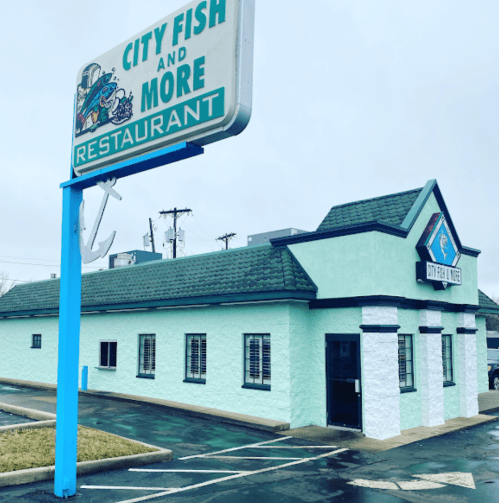 Exterior of City Fish and More restaurant, featuring a teal building and a large sign, on a cloudy day.