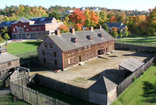 A historic wooden building surrounded by a wooden fence, set against a backdrop of colorful autumn trees.