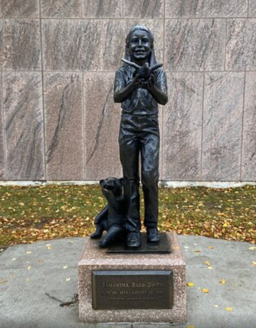 Statue of a young girl holding a bird, with a dog beside her, commemorating Samantha Reed Smith.