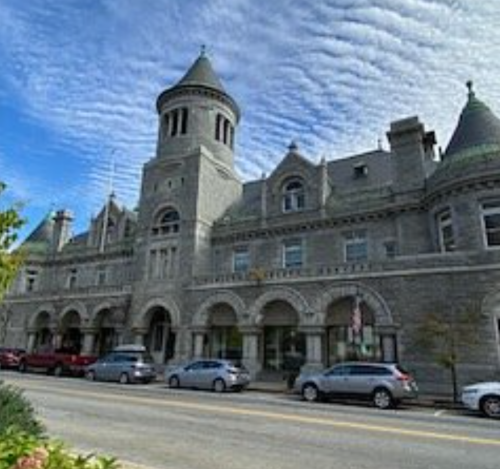 Historic stone building with turrets and arched windows, set against a blue sky with scattered clouds.