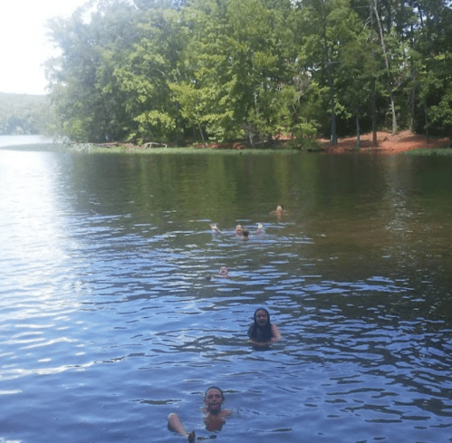 A group of people swimming in a calm lake surrounded by lush green trees.