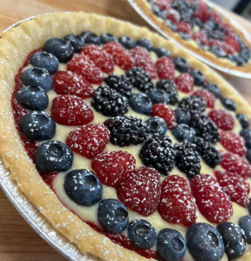 A close-up of a fruit tart topped with blueberries, raspberries, and blackberries on a creamy filling.