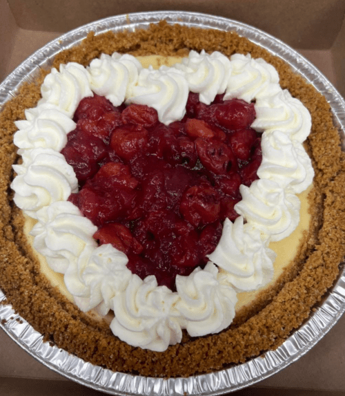 A heart-shaped cheesecake topped with cherry filling and whipped cream, in a graham cracker crust.