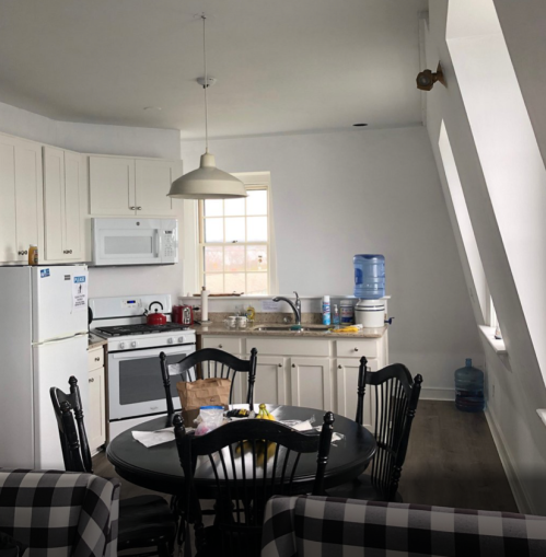 A bright kitchen with white cabinets, a round table, and a water cooler, featuring modern appliances and a cozy atmosphere.