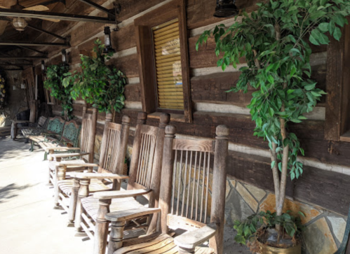 A rustic porch with wooden rocking chairs and potted plants against a log cabin wall.