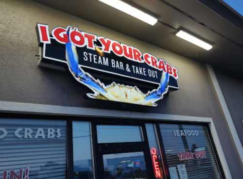 Sign for "I Got Your Crabs" Steam Bar & Take Out, featuring a crab graphic and bright lights. Open for seafood takeout.
