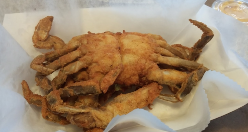 A fried soft-shell crab served on a white paper-lined plate.
