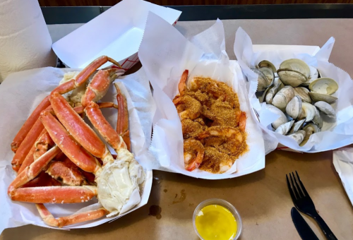 A table with three seafood dishes: crab legs, breaded shrimp, and clams, accompanied by a small container of dipping sauce.