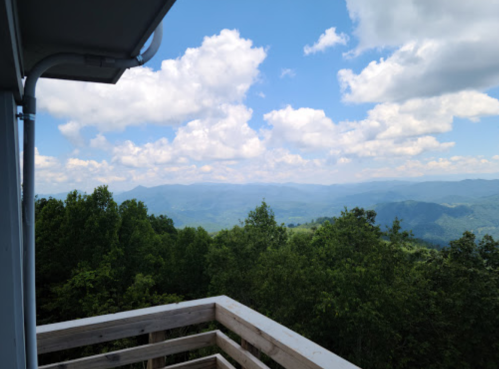 A scenic view from a balcony overlooking lush green mountains and a blue sky filled with fluffy clouds.