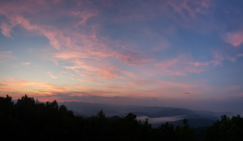 A panoramic view of a colorful sunset sky over distant mountains and a misty valley.