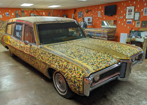 A colorful, beaded hearse displayed in a room with orange walls and various memorabilia.