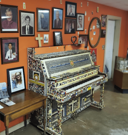 A colorful, decorated piano against an orange wall, surrounded by various framed photos and a mirror.