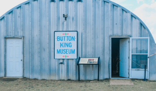 Exterior of the Button King Museum, featuring a large sign and two doors, set against a blue sky.