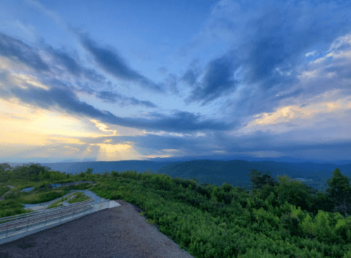 A panoramic view of a mountainous landscape under a dramatic sky with clouds and a hint of sunset.