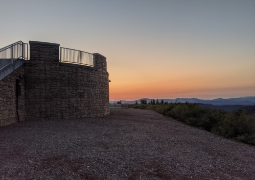 A stone observation tower at sunset, with a colorful sky and distant mountains in the background.