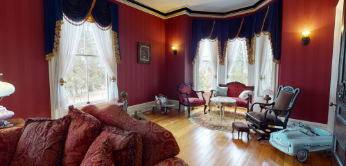 A cozy, elegantly furnished room with red walls, vintage furniture, and large windows draped in blue curtains.