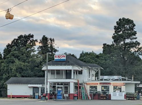A vintage Exxon gas station with a two-story building, surrounded by trees and a cloudy sky.