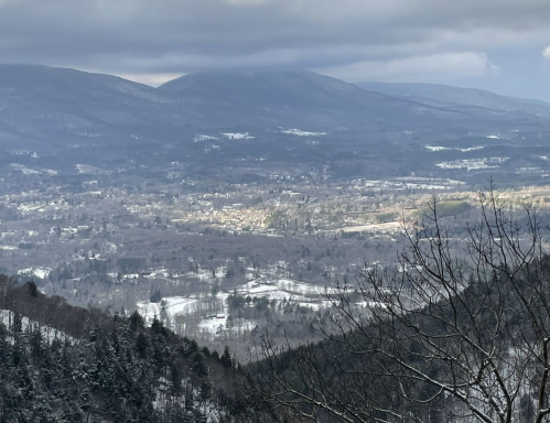 A scenic view of a snowy valley surrounded by mountains under a cloudy sky.