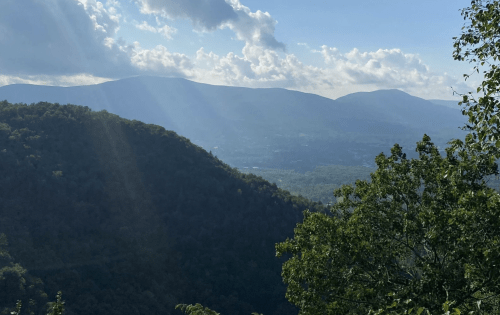 A scenic view of mountains under a blue sky with clouds, featuring sunlight streaming through the landscape.