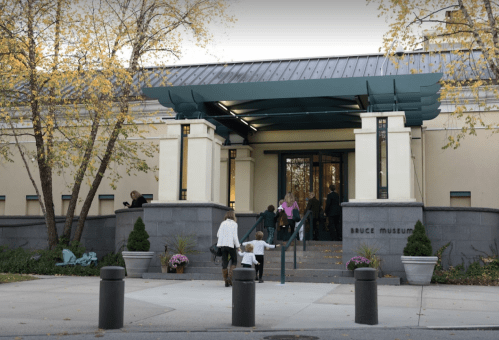 People entering the Bruce Museum, surrounded by trees and autumn foliage, with steps leading up to the entrance.