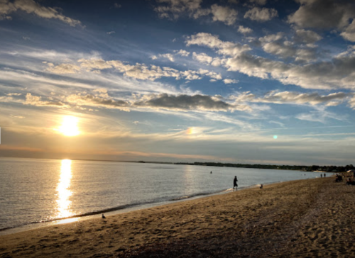 A serene beach at sunset, with golden skies reflecting on calm waters and a few people walking along the shore.