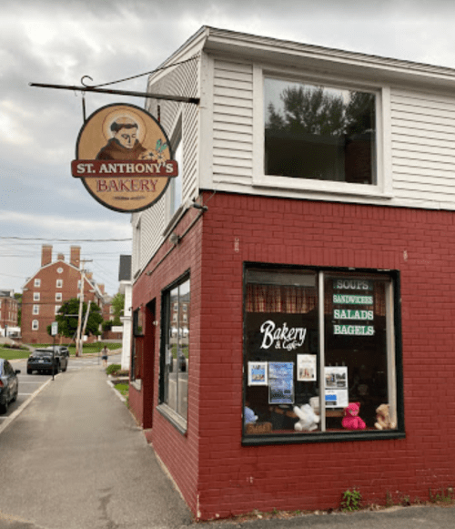 Exterior of St. Anthony's Bakery, featuring a sign and a window displaying menu items like soups, salads, and bagels.
