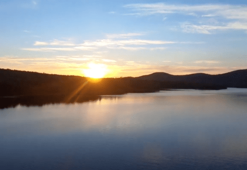 A serene sunset over a calm lake, with mountains silhouetted against a colorful sky.