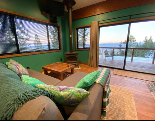 Cozy living room with green walls, a wood stove, and a view of mountains through large windows.